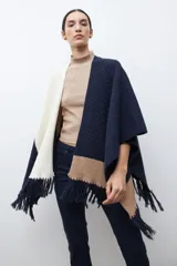 Ruana de tejido de punto con diseño color block en tonos crudo, gris y negro, con terminación de flecos en el ruedo y textura en relieve.