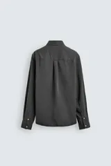 Camisa de corte relajado confeccionada en una mezcla de lyocell y algodón con efecto lavado. Presenta cuello solapa, manga larga con puños abotonados, bolsillo de plastrón en el pecho y cierre frontal con botones.