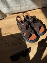 Sandalias de cuero marrón con textura de cocodrilo, diseño de tiras cruzadas con tachas metálicas plateadas y suela track negra de plataforma.