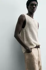 Chaleco de punto color blanco roto, con cuello redondo y sisa, confeccionado en tejido calado de estructura abierta y acabado en rib.
