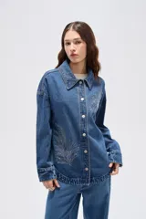 Sobrecamisa de jean azul medio, de corte oversize, con mangas largas y detalles de tachas decorativas en la parte frontal y trasera.