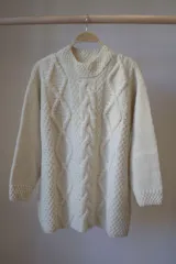 Sweater color crudo tejido a mano en lana merino, con diseño de trenzas en el frente.