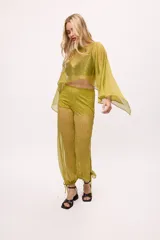 Pantalón ancho de seda color lima, con efecto brillante y textura plisada. Presenta un corte holgado con puños ajustables mediante cintas en los tobillos.