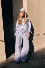 Pijama de dos piezas de algodón a rayas celestes y blancas, compuesto por una camisa de manga larga con botones y ribetes marrones, y un pantalón largo de corte recto con elástico en la cintura.