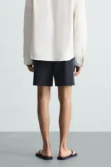 Bañador largo negro con cintura elástica ajustable mediante cordón. Presenta un panel lateral con estampado de cuadros en tonos azul y negro. Incluye bolsillos frontales y un bolsillo trasero con solapa.