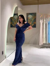 Vestido largo de fiesta en color azul, confeccionado en tela con textura arrugada. Presenta un diseño con escote tipo bardot con nudo central, hombros descubiertos y corte ajustado al cuerpo con una abertura lateral en la falda.