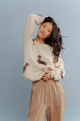 Buzo de lana merino color crema, con diseño tejido de llamas en tonos marrones. Presenta cuello redondo, mangas largas con hombros caídos y puños acanalados.