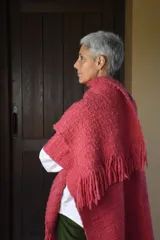 Ruana de lana merino tejida en telar, con diseño de rayas verticales en tonos crudo y rojizo, y terminación de flecos en el ruedo.