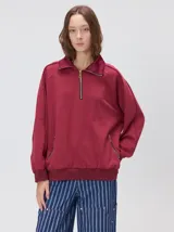 Buzo de algodón color bordó, con cuello polo y cierre frontal parcial. Presenta bolsillos laterales con cierre metálico, mangas largas y corte oversize.