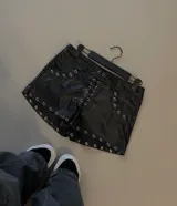 Short negro de tiro medio con cordones entrecruzados en la parte frontal, decorado con múltiples ojales metálicos en los bolsillos y en todo el ruedo.