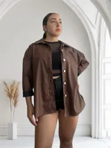 Sobrecamisa color chocolate de cuero sintético con cuello clásico, cierre frontal con botones a presión plateados, bolsillo de parche en el pecho y puños con botón.