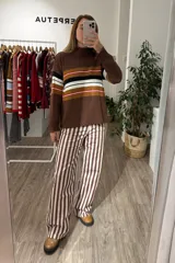Sweater de tejido de punto con cuello alto y mangas largas. Presenta un diseño de rayas horizontales en tonos marrón, negro, blanco y mostaza en la parte frontal y en las mangas.