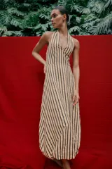 Vestido midi de corte globo con estampado de rayas verticales, cuello halter anudado, escote en pico y espalda descubierta. Presenta bajo abullonado con elástico interior y cierre lateral con cremallera oculta.