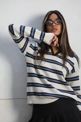 Sweater de punto con diseño a rayas horizontales en tonos blanco, azul y marrón. Presenta cuello tipo polo con solapa en color marrón sólido, mangas largas y puños acanalados.