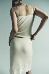 Falda midi de tejido ligero color crema o beige muy claro, con cintura elástica de color beige más oscuro. El bajo está adornado con una aplicación de encaje floral a tono.