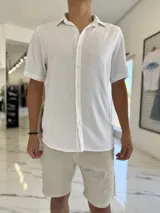 Camisa blanca de manga corta, cuello camisero y cierre frontal de botones.