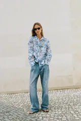Camisa de manga larga con cuello solapa y cierre frontal de botones, confeccionada en tejido combinado semitransparente con estampado floral en tonos azules y blancos.