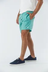 Short de baño liso color turquesa, con cintura elástica y cordón ajustable. Cuenta con bolsillos laterales y logo de la marca en goma en la parte inferior.