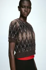 Chaqueta de punto de manga corta y cuello redondo, con cierre frontal de botones y diseño de rombos en tonos marrones, negros y blancos.
