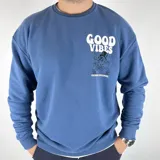 Buzo azul de algodón peletizado, corte oversize, con cuello redondo y mangas largas. Estampa frontal con texto "Good Vibes" y dibujo de un personaje. Estampa trasera con el mismo diseño.