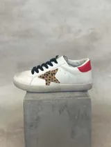 Zapatillas bajas blancas con cordones negros, estrella de animal print y detalle rojo en el talón.