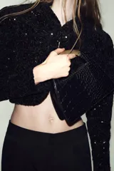 Bolso de mano negro con textura de cocodrilo en relieve, doble asa metálica dorada y cadena bandolera extraíble. Cuenta con cierre de cremallera y bolsillo interior con cremallera.