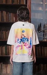 Remera blanca de manga corta y cuello redondo, de calce oversize. Presenta una estampa frontal inspirada en el tarot, con una mujer sentada en un paisaje surrealista, estrellas y la frase "LE ÉTOILE".