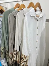 Vestido camisero largo de lino blanco con botones, cuello clásico y mangas largas con puños estampados con animal print. Tiene un corte irregular con el frente más corto que la parte trasera y estampado animal print en el ruedo.