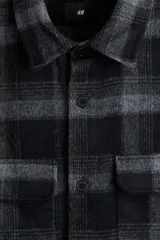 Sobrecamisa de franela con patrón de cuadros en tonos negro y gris. Presenta cuello inglés, tapeta lisa con botones, dos bolsillos superiores con solapa y mangas largas con puños abotonados.