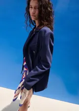 Blazer azul marino de estilo sastrero, corte recto, con cuello pico y solapas de muesca. Cuenta con dos bolsillos con solapa en los laterales y cierre frontal de doble botonadura.