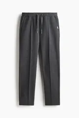 Pantalón tipo jogger de punto en tono gris oscuro, con cintura elástica y cordón ajustable. Presenta un pliegue cosido en el frente de cada pierna, bolsillos laterales y un bolsillo insertado trasero.