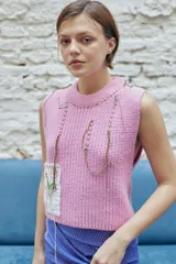 Chaleco tejido color rosa con cuello redondo, sisas amplias, largo cropped y parche bordado a mano con flores.