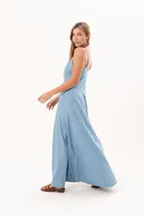 Vestido largo de denim fino y liviano, color celeste, con breteles finos, escote delicado, silueta entallada en la parte superior, falda amplia con recortes verticales y bolsillos laterales.