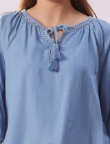 Blusa celeste de tencel con cuello redondo, escote en V y lazo de ajuste. Tiene cuello y escote calado y mangas 3/4 amplias con puño elastizado.