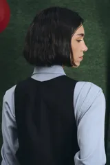 Mono largo de color negro con cierre frontal de botones vintage de distintos colores. Presenta un diseño sin mangas, con bolsillos laterales y una cinta para herramientas en la parte trasera.