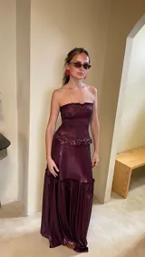 Vestido largo strapless de lamé elastizado color bordó, con cuerpo fruncido tipo corsel y falda larga amplia con volados y frunces.