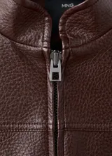 Chaqueta estilo bomber de cuero sintético marrón oscuro, con cierre frontal de cremallera, cuello alto abotonado y bolsillos frontales con solapa.