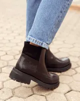 Botinetas de cuero negro con suela track dentada. Presentan una combinación de texturas en el lateral, con una sección de cuero liso y otra con textura grabada, además de un panel elástico en la parte superior del tobillo.