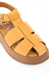 Sandalia tipo guillermina de cuero color camel, con diseño de tiras anchas entrelazadas, cierre con hebilla metálica lateral y suela de plataforma plana en tono marrón.