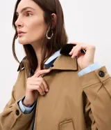 Campera Comfort de poliéster color camel, con cuello de poliuretano en contraste color marrón oscuro, cierre frontal y bolsillos con solapa y botones. Presenta martingalas en los hombros y elástico en la cintura.