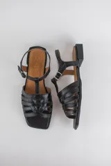 Sandalias de cuero color negro, de suela plana, con tiras entrelazadas en la capellada y tira ajustable en el talón con hebilla metálica.