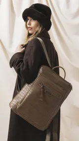 Mochila marrón con textura símil cocodrilo, compartimento principal con cierre, amplio bolsillo frontal con cierre y correas ajustables de tela.