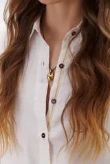 Camisa beige de manga larga con botones marrones y cuello clásico. Presenta un detalle de costura dorada a lo largo de la botonera.