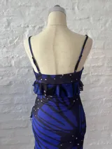 Vestido corto de microtul con estampado de mariposas azules y negras sobre fondo negro. Tiene breteles finos, escote en V con volados y falda con volados y abertura lateral.