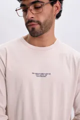 Remera manga larga de color beige, con cuello redondo y pequeña estampa de texto en el pecho.