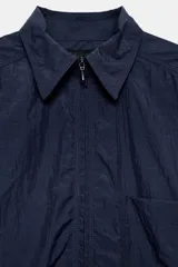 Camisa oversize de nylon color azul marino, con cuello solapa, manga larga, bolsillo de parche en el pecho y cierre frontal con cremallera.