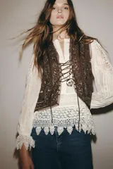 Blusa blanca de algodón con cuello redondo, manga larga con volante en el puño y detalle de bordados y aplicaciones de encaje en paneles geométricos. Cierre frontal con botones.