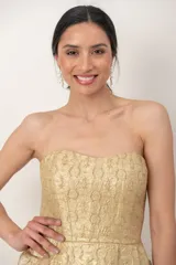 Vestido corto strapless de brocato dorado, con escote recto, corte entallado en la cintura, falda con tablas y bolsillos laterales.