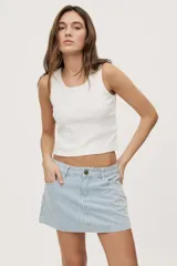 Falda corta de jean con diseño a rayas verticales celestes y blancas. Presenta tiro medio, bolsillos delanteros, pasadores en la cintura y cierre frontal con botón metálico.