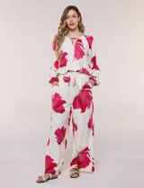 Conjunto de dos piezas de crep compuesto por una blusa holgada con escote en V y mangas largas abullonadas, y un pantalón palazzo tiro alto con pretina elástica. Presenta un estampado floral en tonos rosados sobre base blanca.